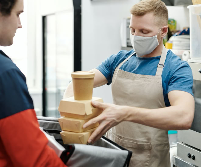 Man Wearing a Face Mask Putting Food on a Thermal Bag